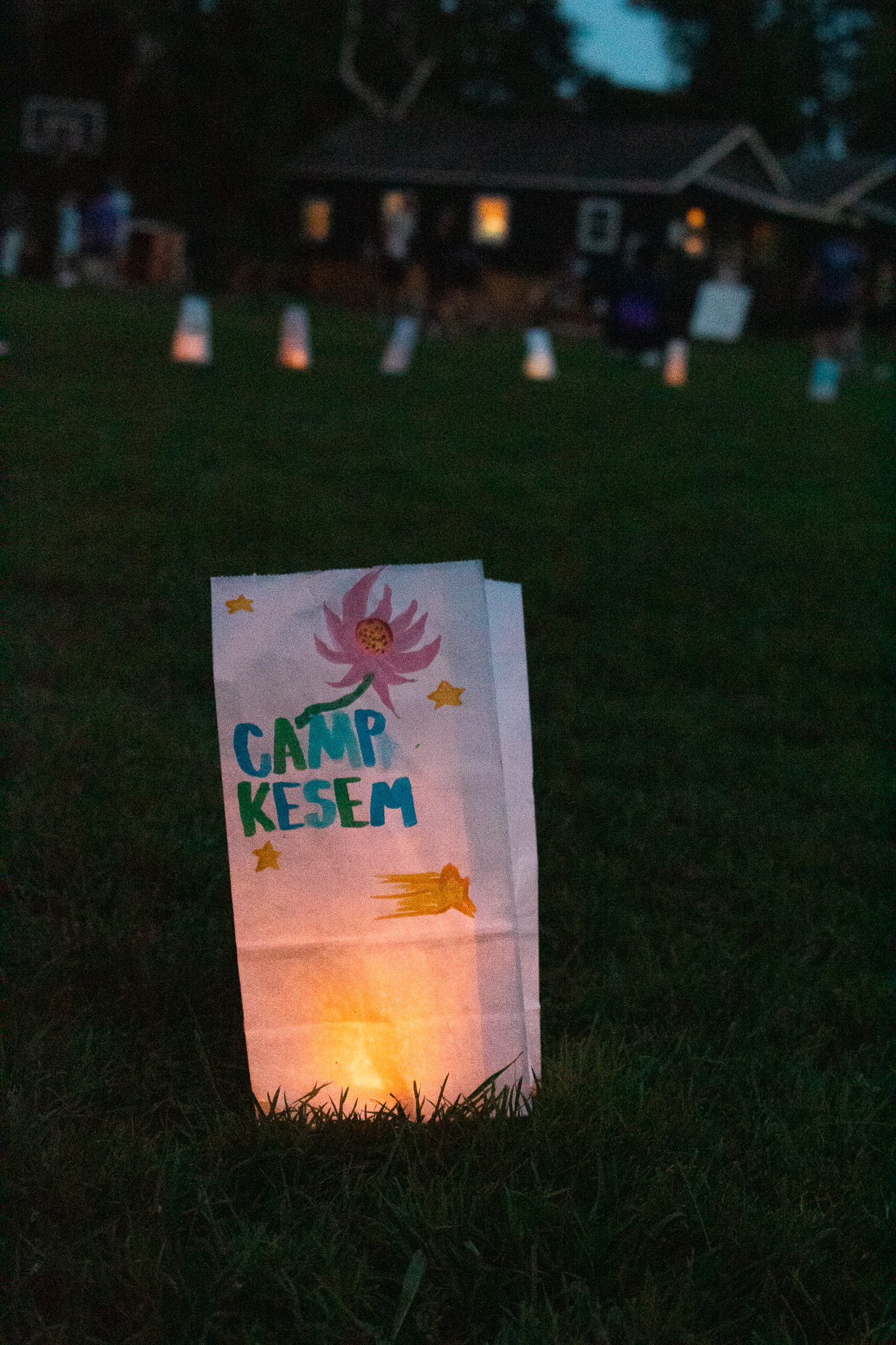 A glowing Camp Kesem paper lantern on the grass at dusk
