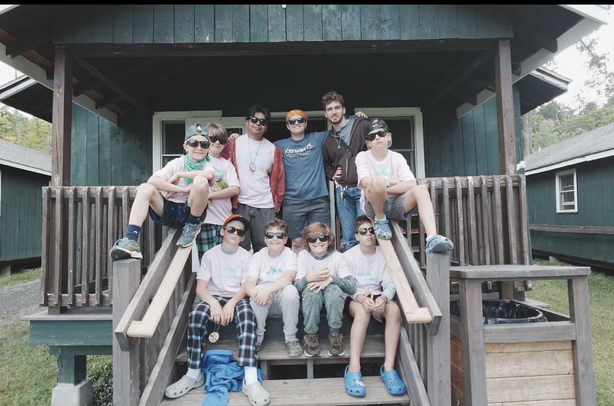 A group posing on the steps of a green camp cabin